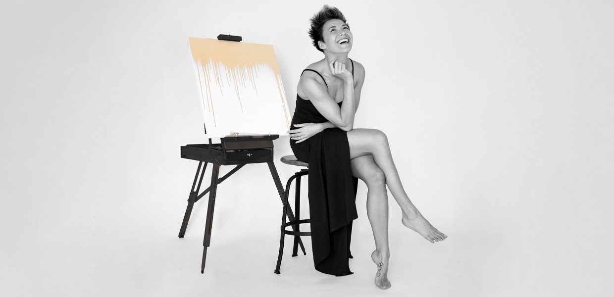 A joyful woman sitting beside an easel with a blank canvas.