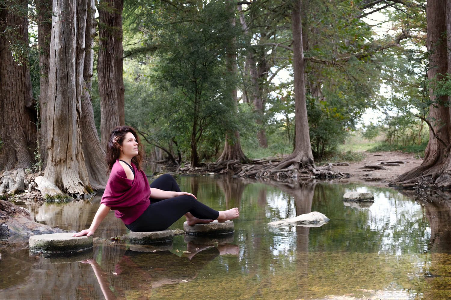 Woman relaxing on a log over a calm river surrounded by trees.