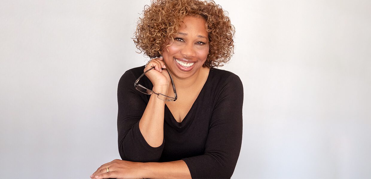 Smiling woman with curly hair in a black top posing against a white background.