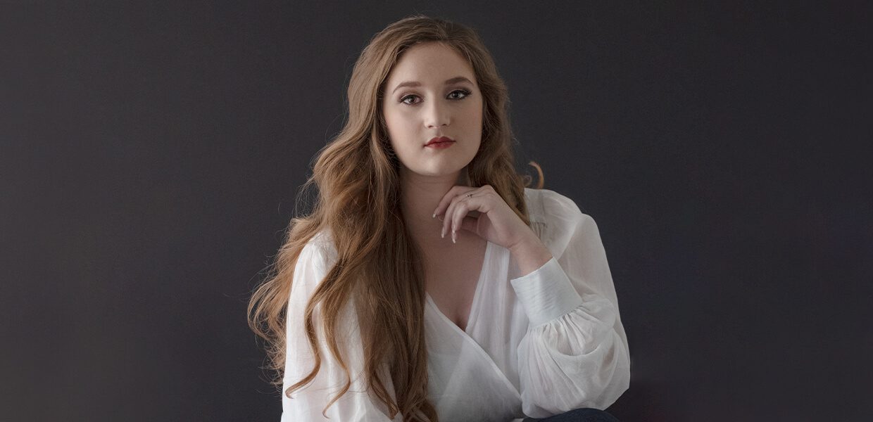 A woman with long wavy hair poses against a dark background.