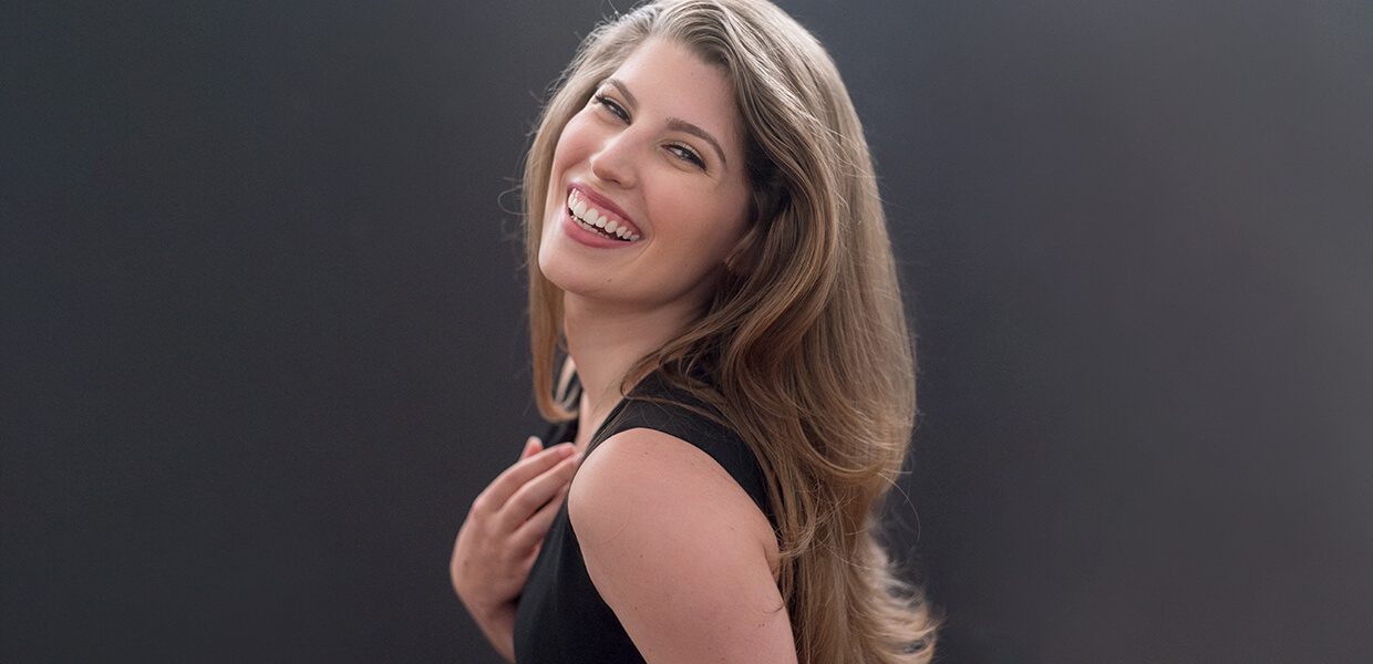 A young woman with long hair smiling joyfully against a dark background.