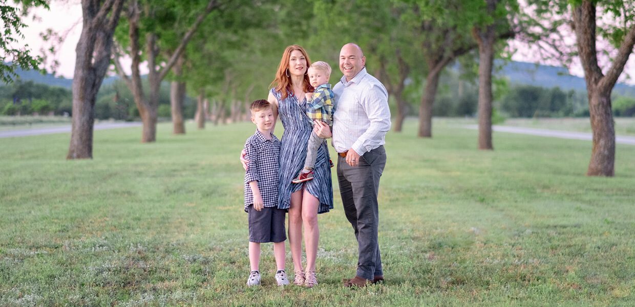 A happy family of four posing outdoors in a park.